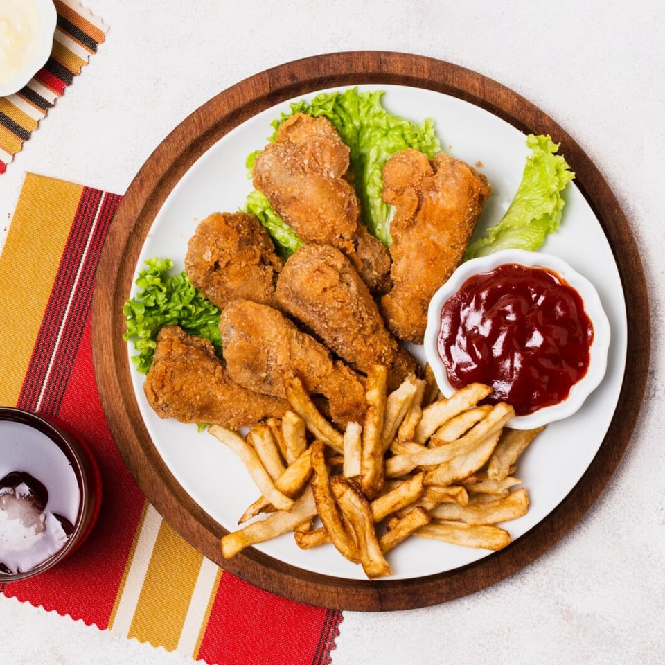 Fried chicken drumsticks and fries with ketchup and lettuce on a white plate.