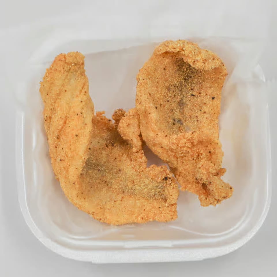 Two pieces of crispy fried fish, seasoned with pepper, in a white takeout container.
