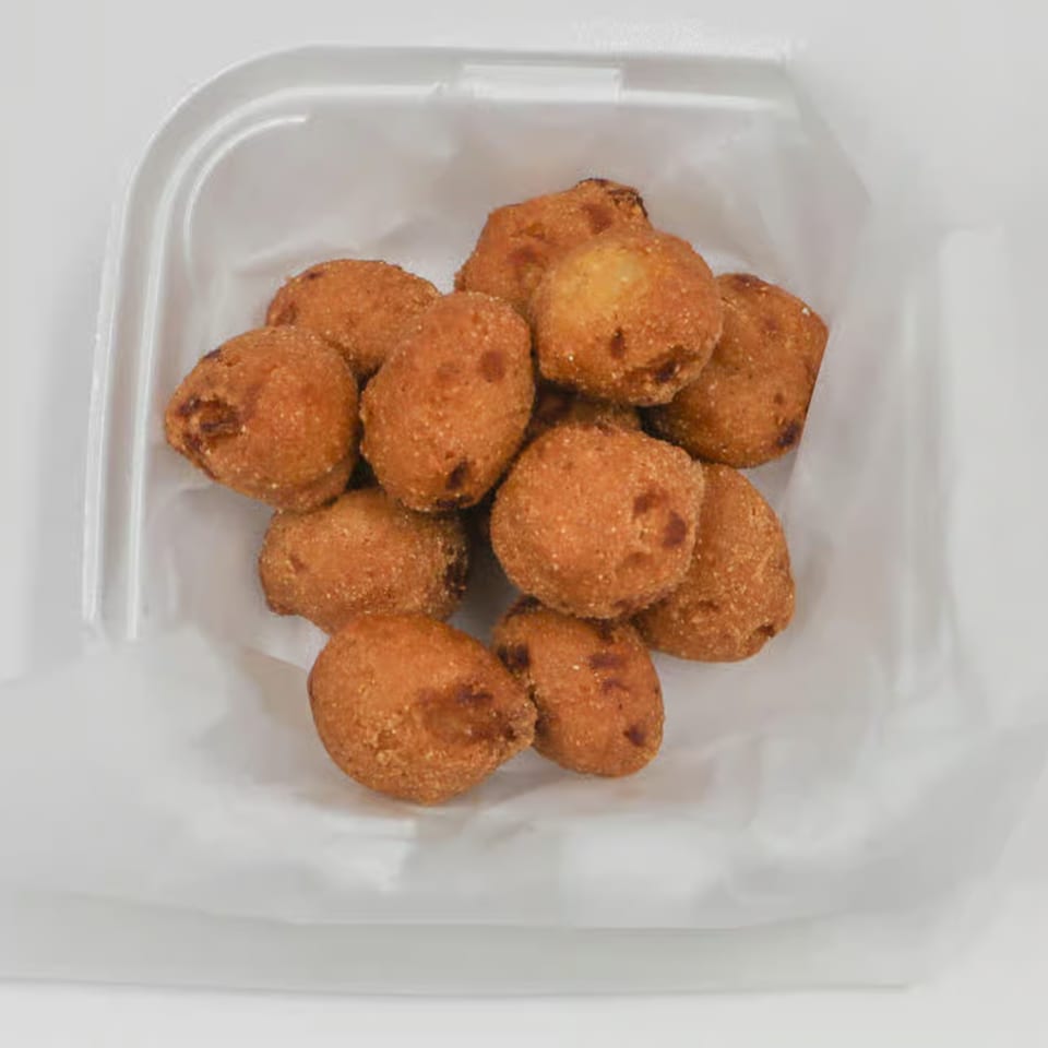 Golden-brown hush puppies, a classic seafood side, served in a white takeout container.