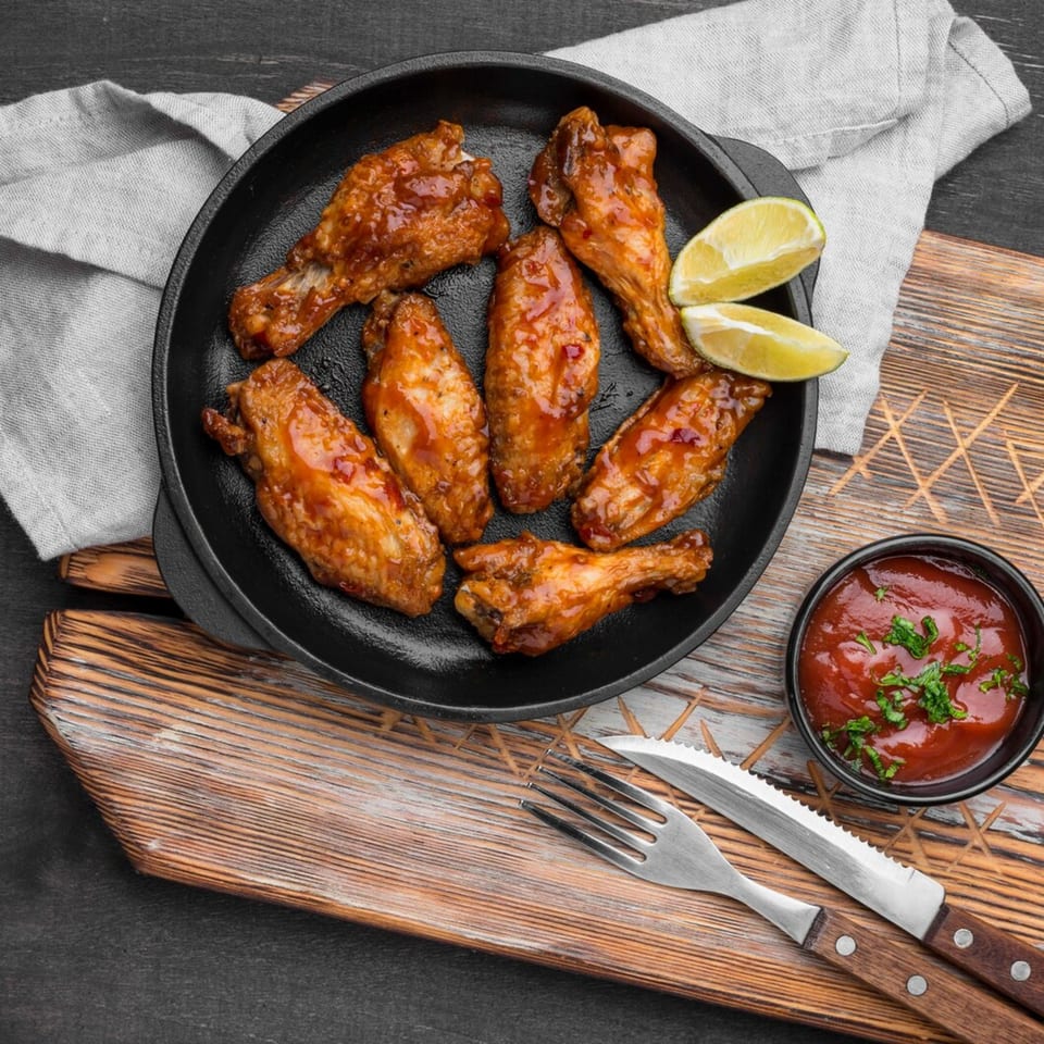 Glazed chicken wings with lime wedges and a side of sauce, on a wooden board.